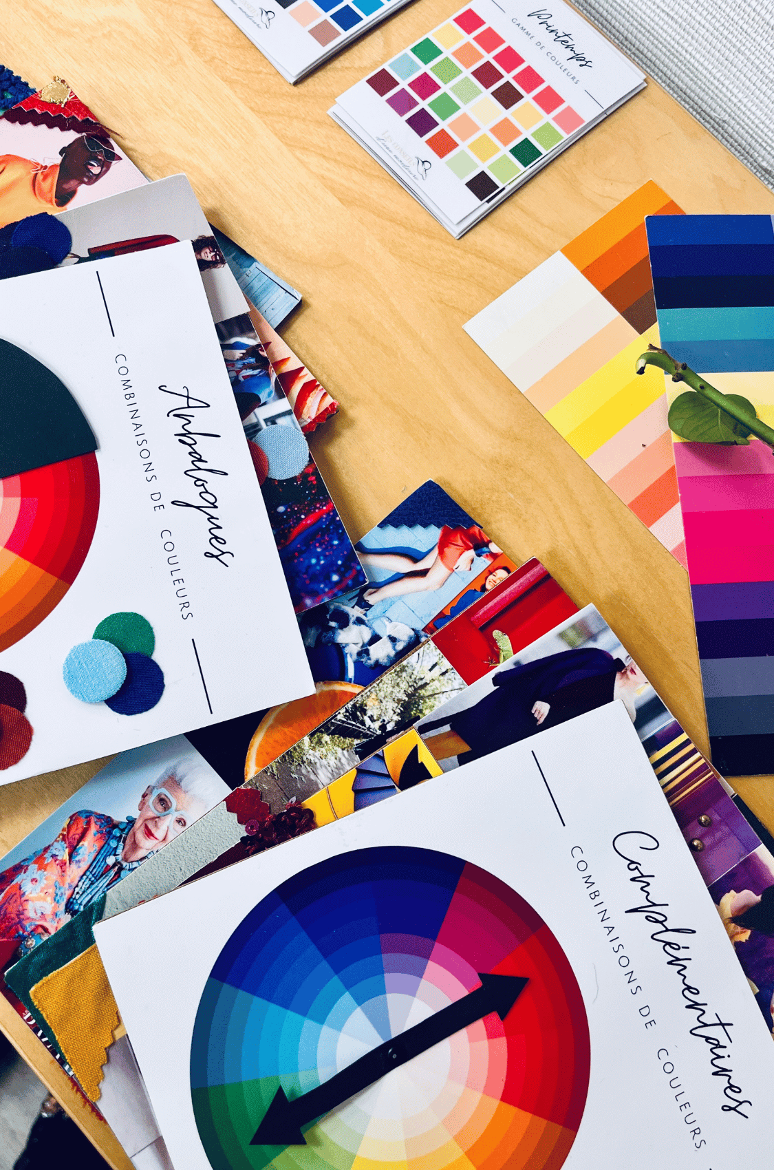 Un bouquet de fleurs séchées repose sur le rebord d’une fenêtre ornée de vitraux colorés représentant des fleurs. Sur une table en bois en contrebas, des tissus de couleurs, des nuanciers, des planches de style de mode sont dispersés, L’image évoque un atelier de conseil en image et de colorimétrie lors d’un week-end féminin ou d’une retraite bien-être.